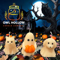 Cream-colored ghost kitty, ghost holding an orange pumpkin, and ghost puppy candles displayed against a moonlit Halloween backdrop.