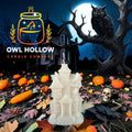 Bone white haunted house candle with detailed windows, peaked roofs, and a front door, displayed against a moonlit Halloween backdrop.