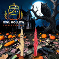 Two Halloween-themed taper candles, one beige with a ghost face and one red with a twisted ribbon design, displayed in front of a spooky digital background featuring an owl, haunted house, pumpkins, and a skeleton. 