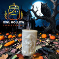 Bone-white pillar candle with a raised long-haired witch design against a Halloween backdrop with pumpkins, a haunted house, and an owl.