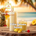 Lit Piña Colada candle with pineapple-yellow wax in a clear glass, beside pineapple pieces and a red cherry, with a tropical beach backdrop and Owl Hollow Candle Company branding.